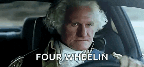 a man in a costume is driving a car and says four wheelin .