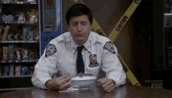 a police officer is sitting at a table eating cereal with a caution tape behind him