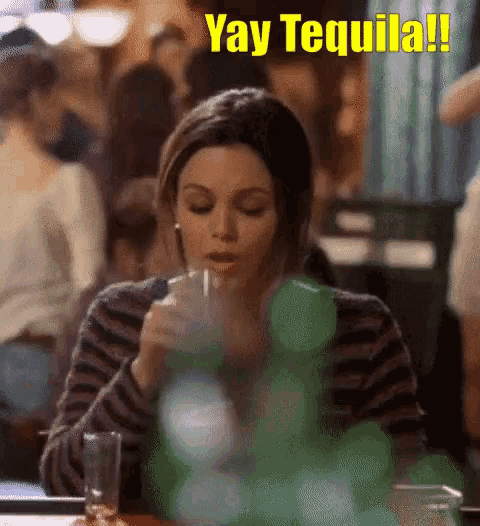 a woman is sitting at a table drinking a shot of tequila .