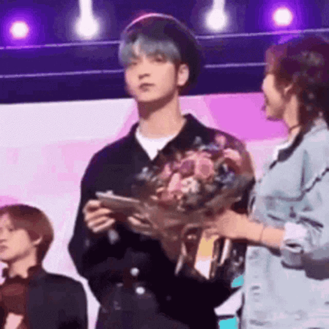 a man is holding a bouquet of flowers while standing next to a woman on stage .