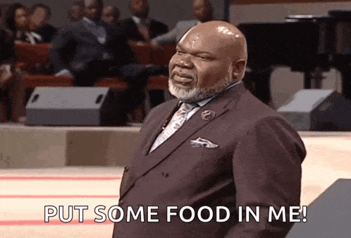 a man in a suit and tie is standing in front of a crowd and saying put some food in me .