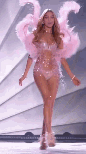 a woman in a pink feathered costume is walking down a runway at a fashion show .
