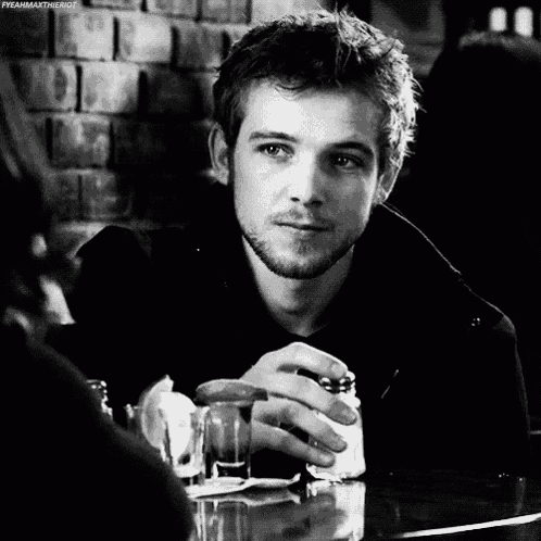 a man with a beard is sitting at a table holding a glass and a cigarette .