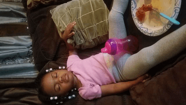 a little girl is sleeping on a bed next to a plate of food and a pink bottle