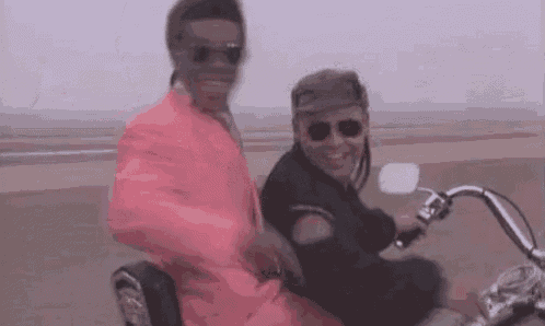a man in a pink suit is riding a motorcycle next to another man .