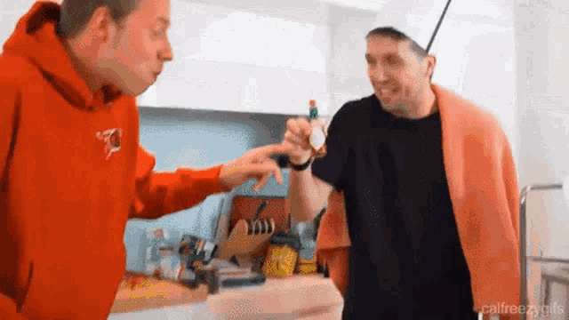 two men are standing in a kitchen and one is wearing a chef 's hat .