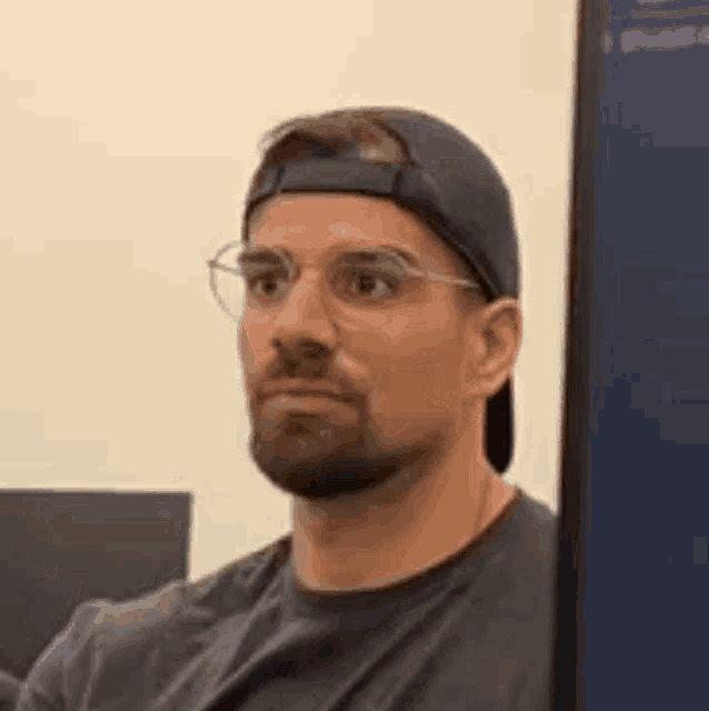 a man wearing glasses and a baseball cap is sitting in front of a computer .