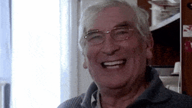 an elderly man wearing glasses and a sweater is smiling .