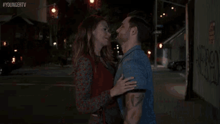a man and a woman are kissing in front of a building on a city street .