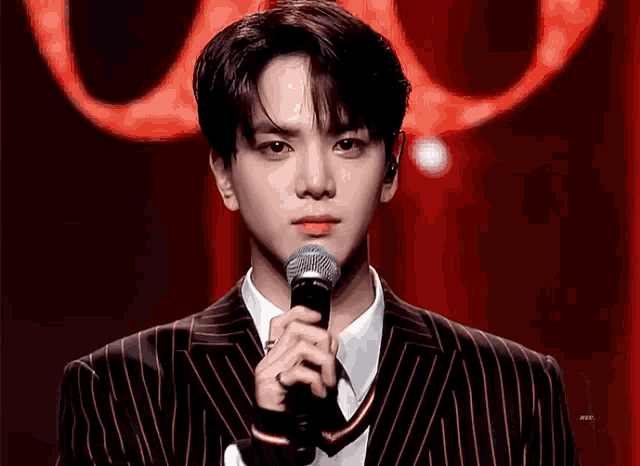 a young man in a suit is holding a microphone in front of him .