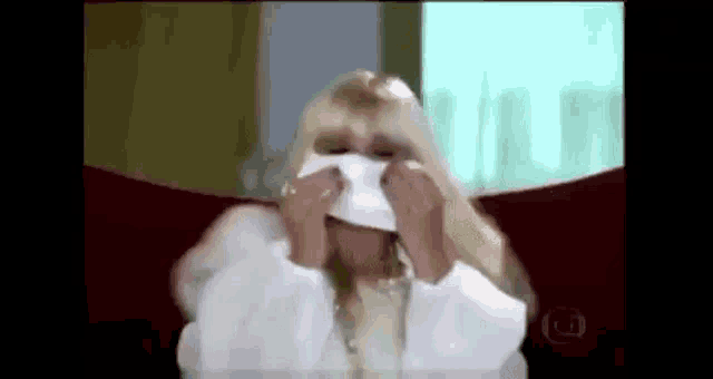 a woman in a white coat is blowing her nose with a tissue .
