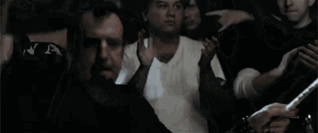 a group of people are standing in a dark room applauding while a man is holding a stick .