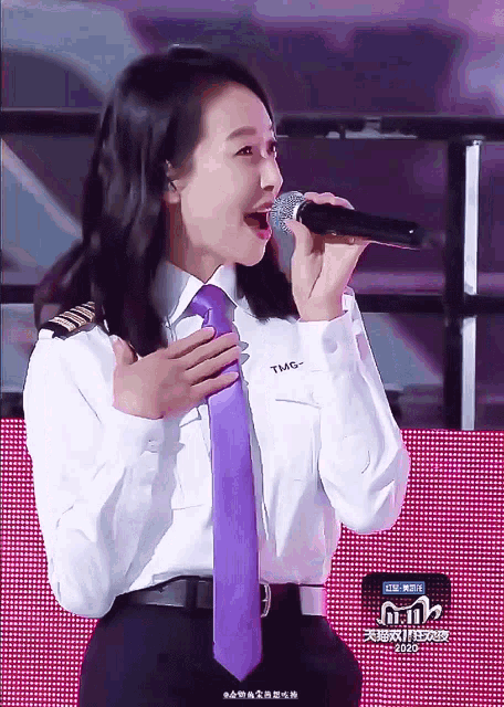 a woman singing into a microphone while wearing a shirt that says tmg