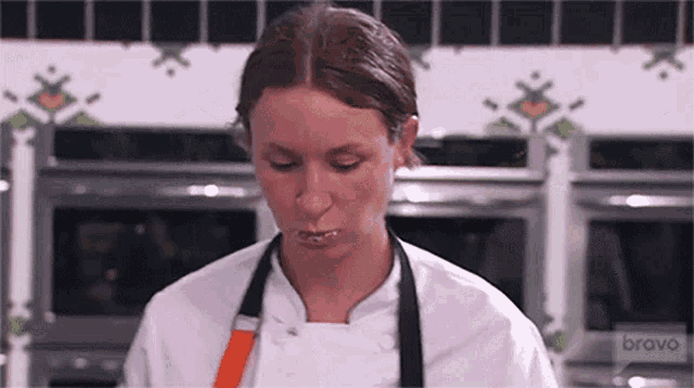 a woman in a chef 's uniform is standing in a kitchen with bravo written on the wall behind her .