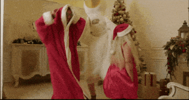 a man and a woman in santa costumes are dancing in a room with a christmas tree