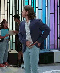 a man in a blue jacket and jeans is standing in front of a rainbow wall