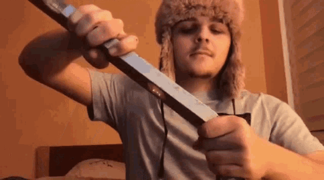 a young man wearing a fur hat is holding a large knife in his hands .