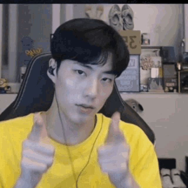 a young man in a yellow shirt is giving a thumbs up sign while sitting in a chair .