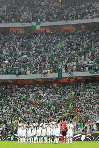 a group of soccer players stand on a field in front of a crowd wearing white jerseys