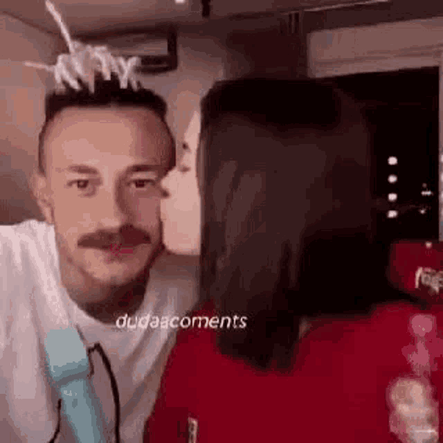 a man with a mustache is kissing a woman on the cheek while holding a microphone .