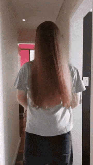 a woman with long hair is standing in a hallway with her back to the camera
