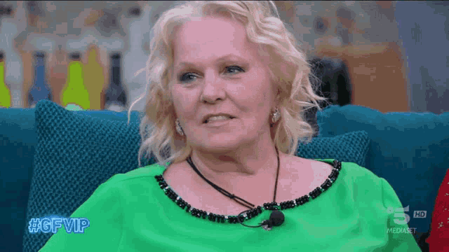 a woman in a green top is sitting on a blue couch with the hashtag #gfvip on the bottom
