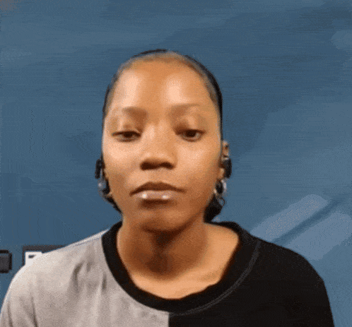 a woman wearing earrings and a black and gray shirt looks at the camera