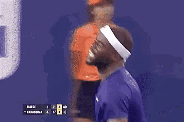 a man wearing a headband is playing tennis while a woman in an orange shirt is standing behind him .