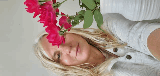 a woman in a white shirt is holding a vase of pink flowers in front of her face