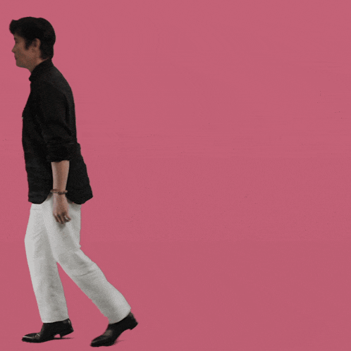 a man wearing a black shirt and white pants is walking on a pink background
