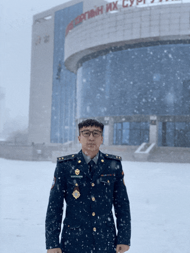 a man in a military uniform stands in the snow in front of a building that says " монголын их сургууль "