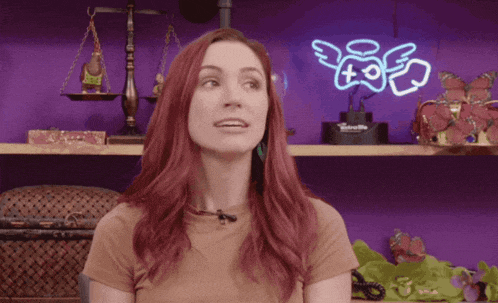 a woman with red hair stands in front of a purple wall with a neon sign that says ' angels ' on it