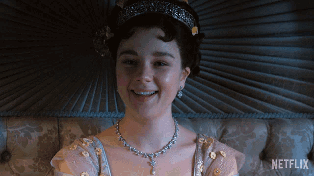 a woman wearing a tiara and a necklace is sitting on a couch with a netflix logo in the corner