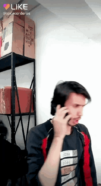 a man talking on a cell phone in front of a shelf with boxes on it that says like
