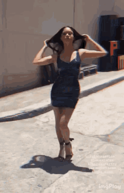 a woman in a blue dress is standing on a sidewalk holding her hair