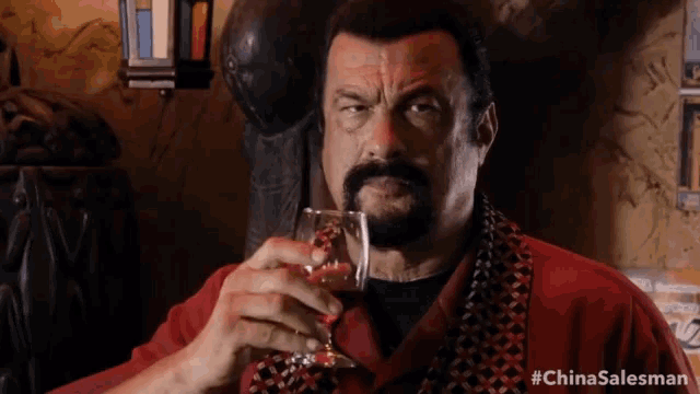 a man in a red shirt is holding a glass of wine with the hashtag #chinasalesman on the bottom