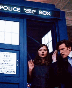a man and a woman are standing outside of a police box