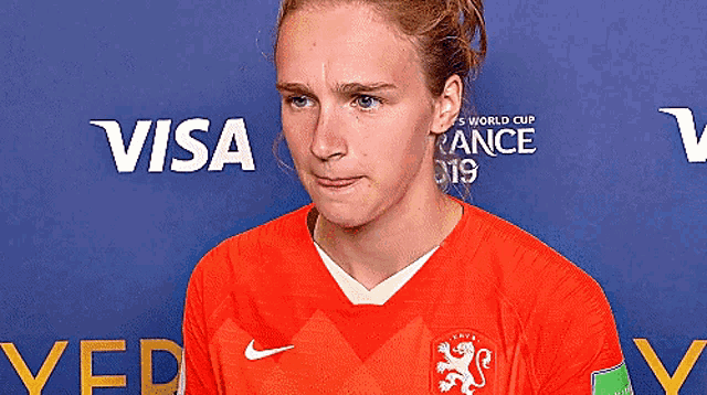 a woman wearing an orange nike jersey stands in front of a visa sign