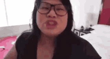 a woman wearing glasses and a black shirt is making a face .