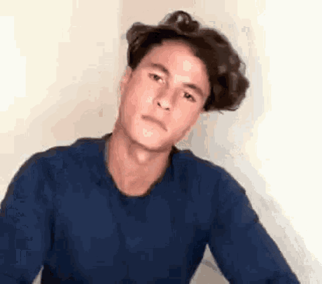 a young man with curly hair wearing a blue sweater is making a funny face .