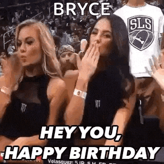 two women are sitting in the stands at a basketball game and one is blowing a kiss .