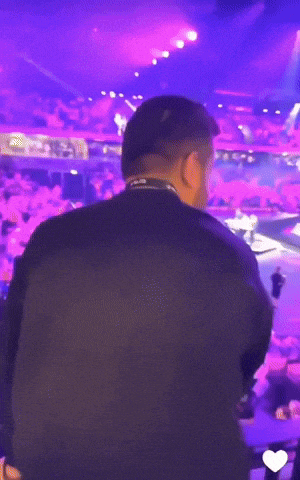 a man in a black shirt stands in front of a crowd with purple lights