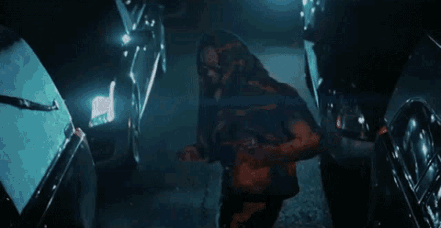 a man in a hooded jacket is standing in a parking lot next to a car .