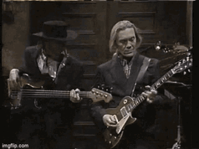 a man in a top hat is playing a guitar next to another man .