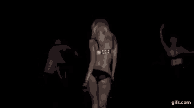 a black and white photo of a woman in a bra dancing in a dark room .