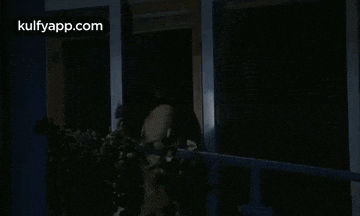 a woman is standing on a balcony at night looking out a window .