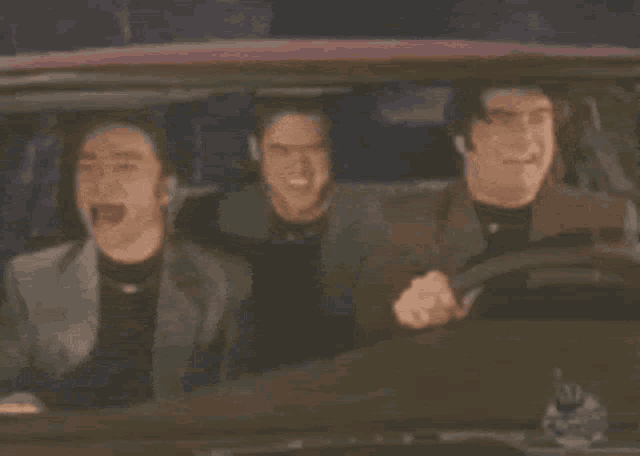 three men are sitting in a car and smiling while driving .