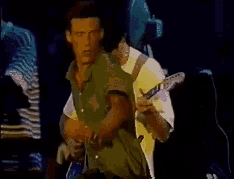 a man in a green shirt is playing a guitar while another man in a white shirt is playing drums .