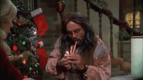 a man is smoking a cigarette with a candy cane in his mouth in front of a christmas tree .