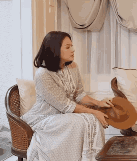 a woman in a white dress is sitting in a chair holding a hat